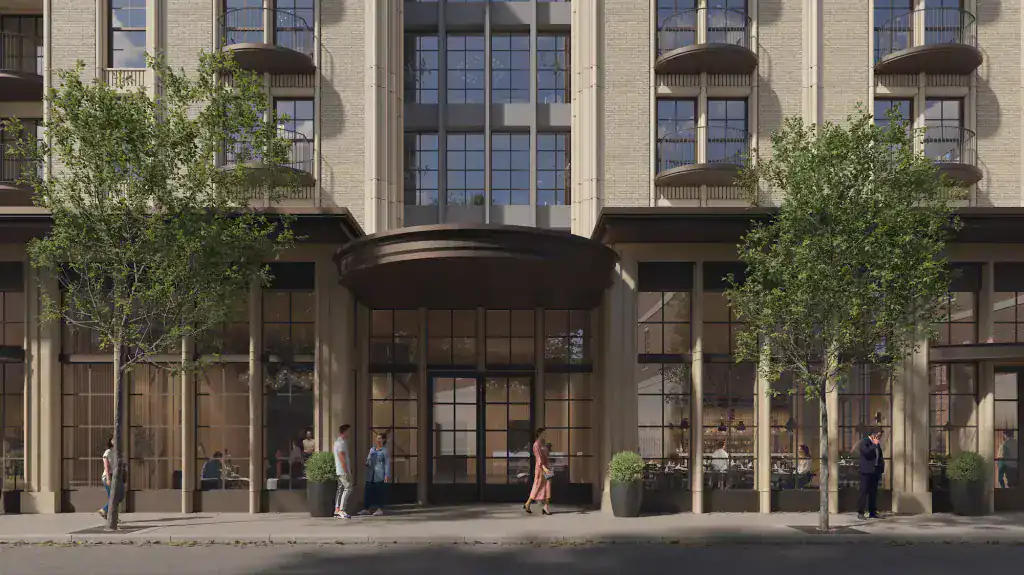 Modern mixed-use building with large glass storefronts and residential balconies, featuring beige brick facade and black window frames.