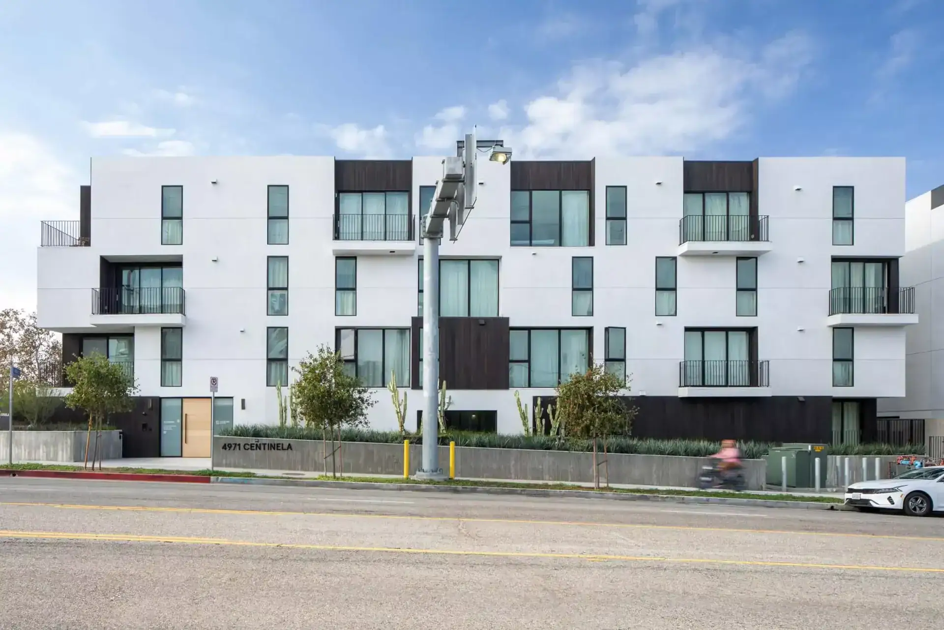 Modern white apartment building with black accents, multiple balconies, and large windows on a city street.