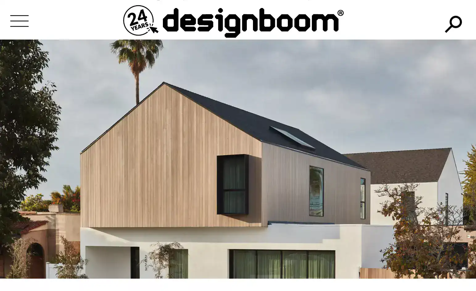 Modern minimalist house with wooden and stucco exterior, gabled roof, large windows, and surrounding trees.