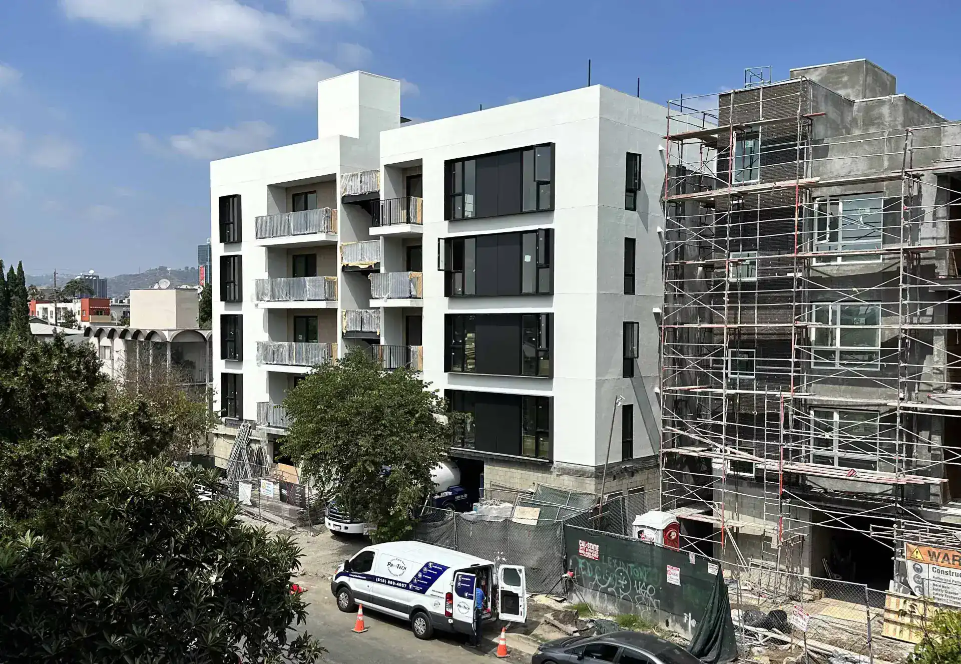 Contemporary white apartment building with large black framed windows and open balconies, modern minimalist style, under construction.