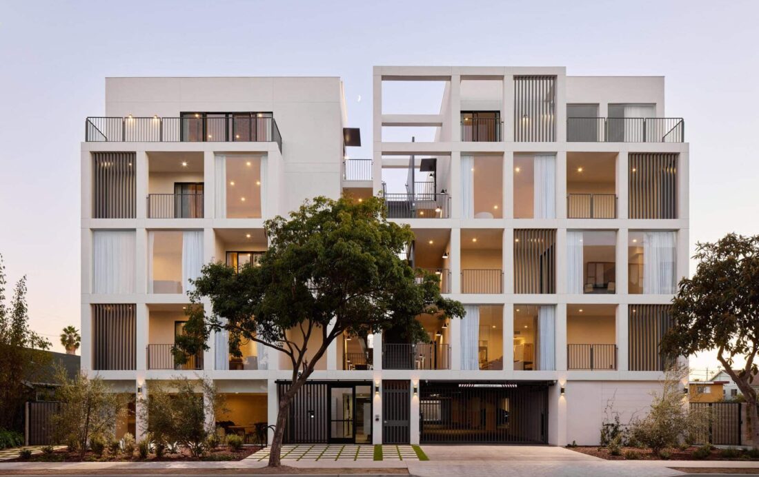 Contemporary white residential building with open balconies, vertical slatted privacy screens, and large glass sliding doors.