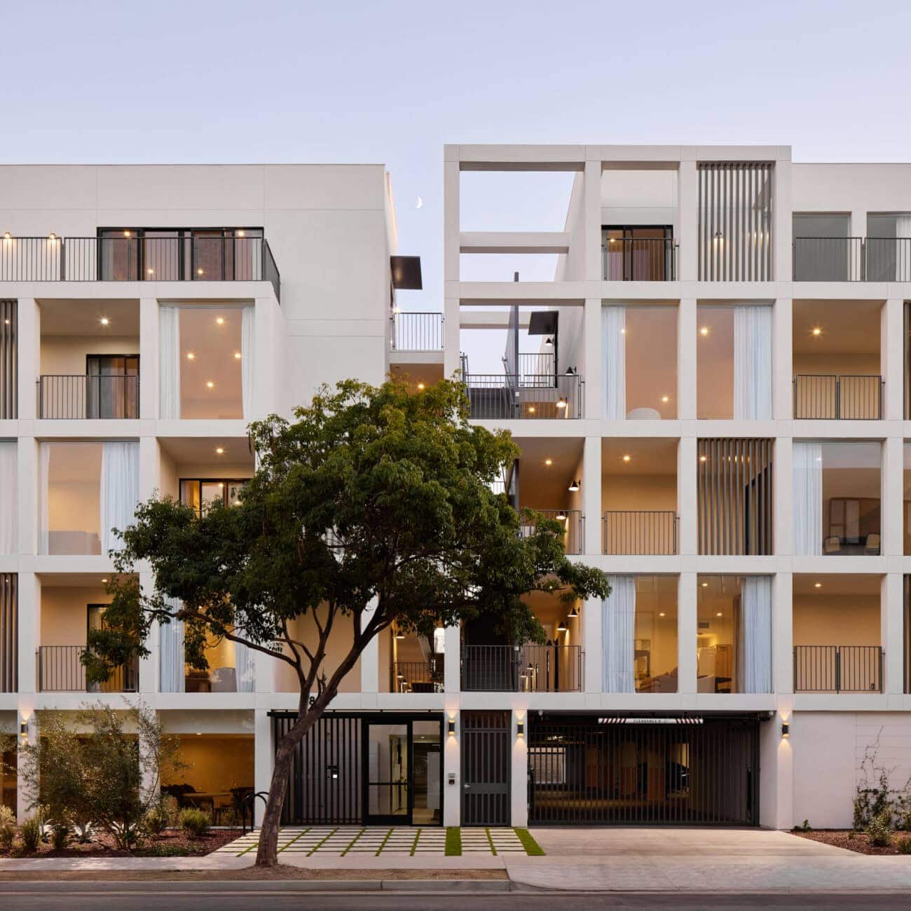 Contemporary white residential building with open balconies, vertical slatted privacy screens, and large glass sliding doors.