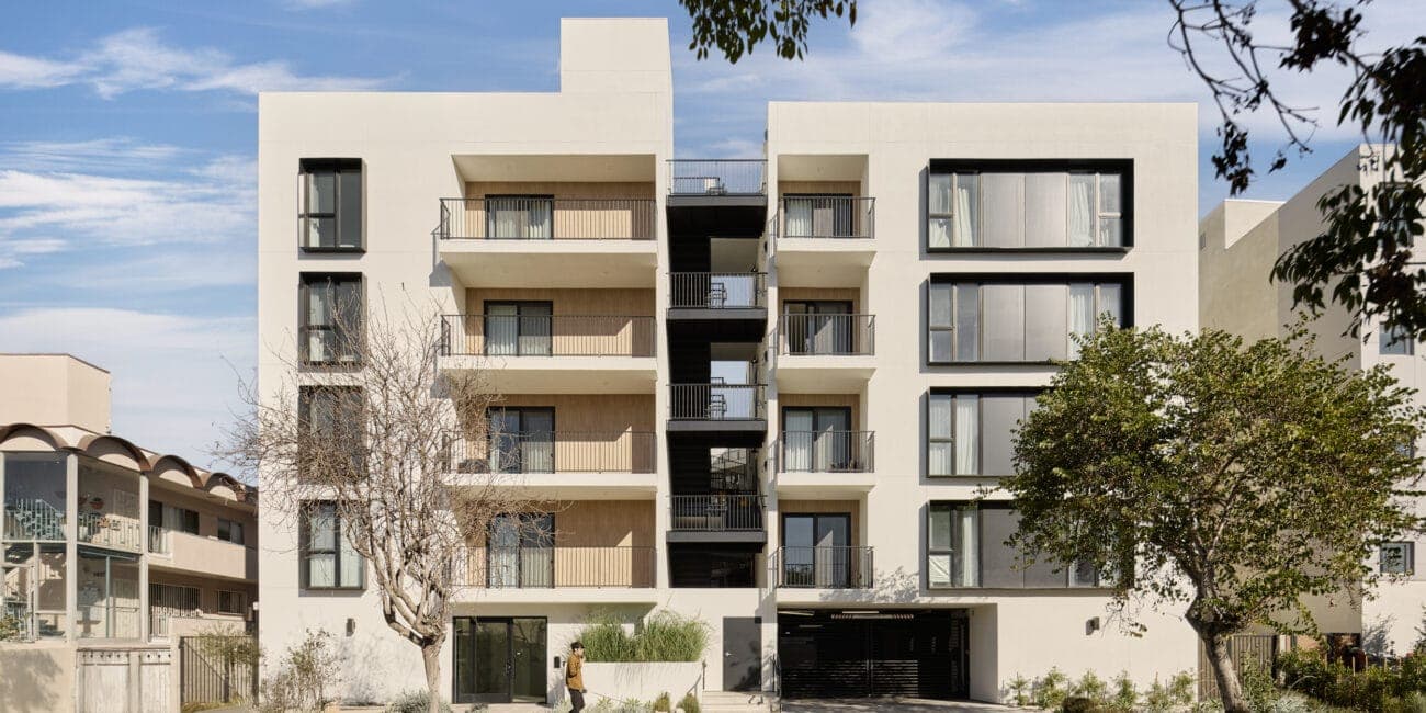Modern multi-story residential building with a minimalist design, white stucco facade, and black window frames.