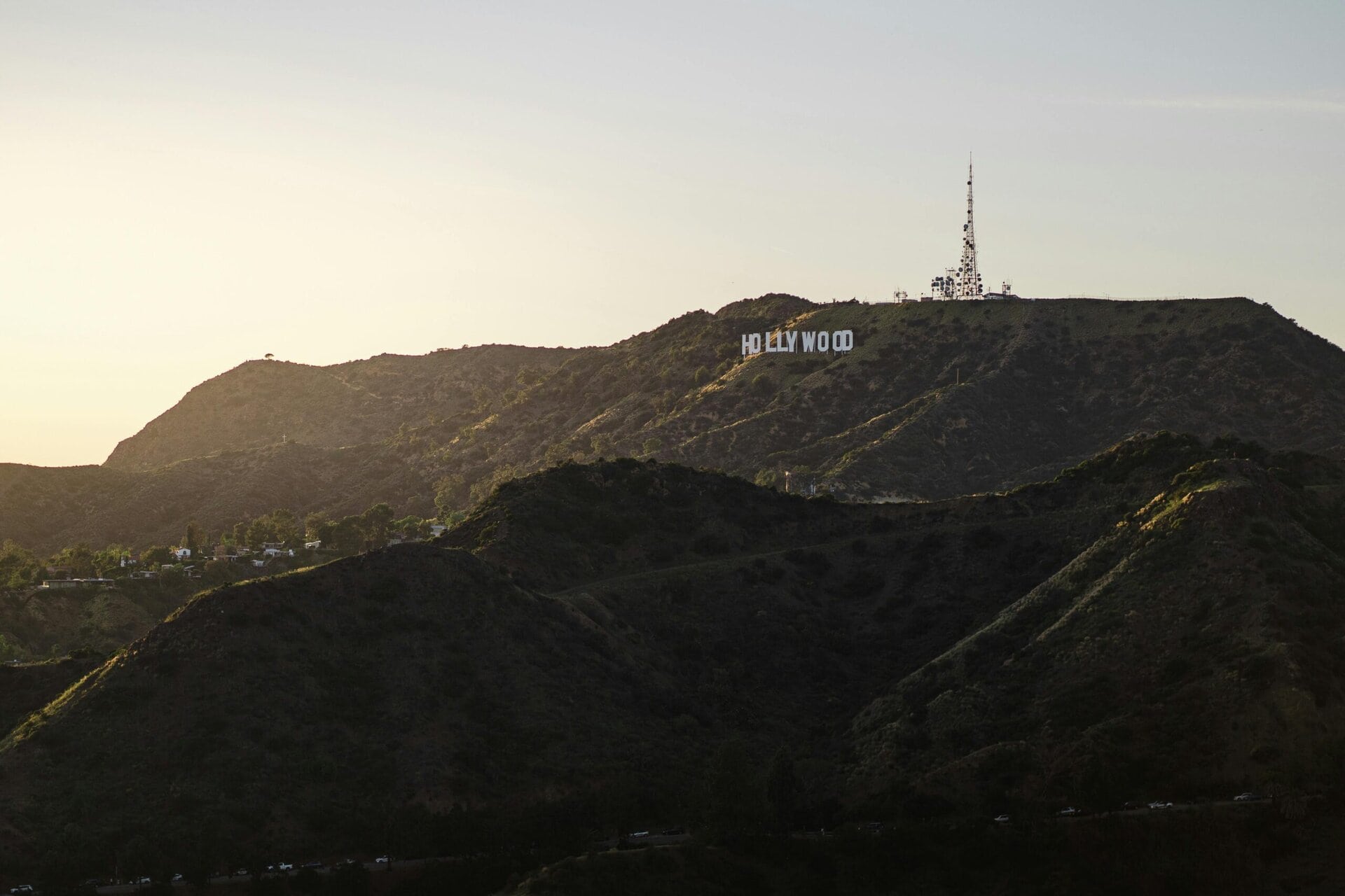 Hollywood sign on a hilly terrain with a communications tower above it, set against a clear sky at sunset.