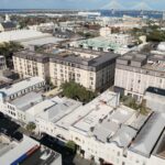 Modern mixed-use building with rooftop terraces, featuring a blend of classic and contemporary architecture, located in an urban setting with a bridge in the background.