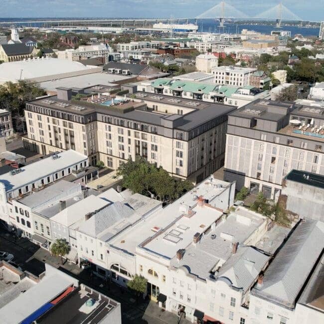 Modern mixed-use building with rooftop terraces, featuring a blend of classic and contemporary architecture, located in an urban setting with a bridge in the background.